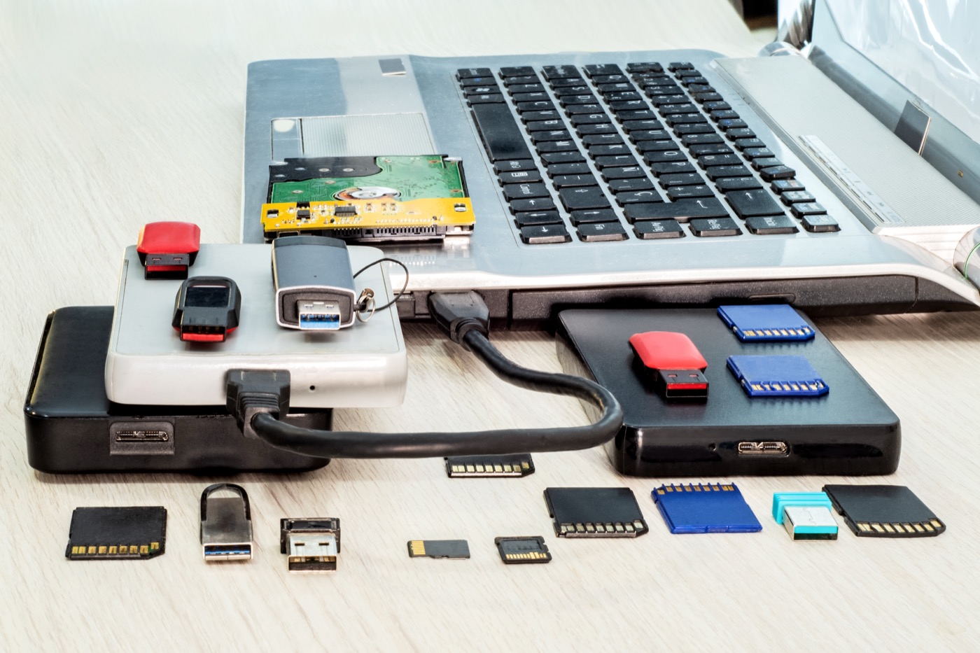 Memory cards, USB sticks and external drives spread around a laptop